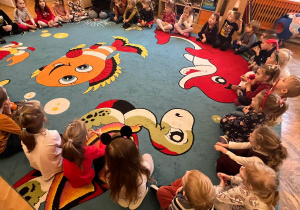 Dzieci siedzą na kolorowym dywanie w kole.